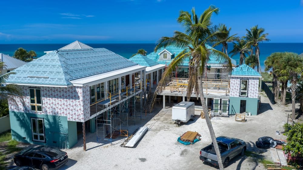 Aerial view of a coastal home under construction with new metal roofing and the Gulf horizon behind