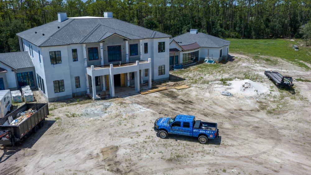Aerial view of a large custom home under construction with a contractor truck on the lot