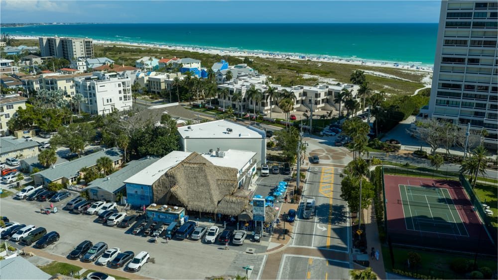 Aerial drone view of a beachfront tiki bar and white sand shoreline on Siesta Key, Florida