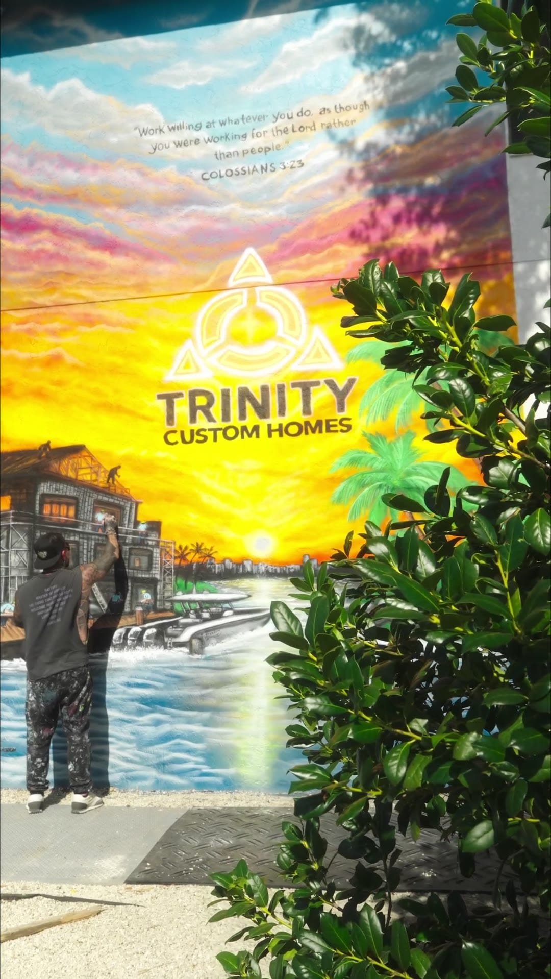 Finished hand-painted sunset mural with the Trinity Custom Homes logo on a building wall