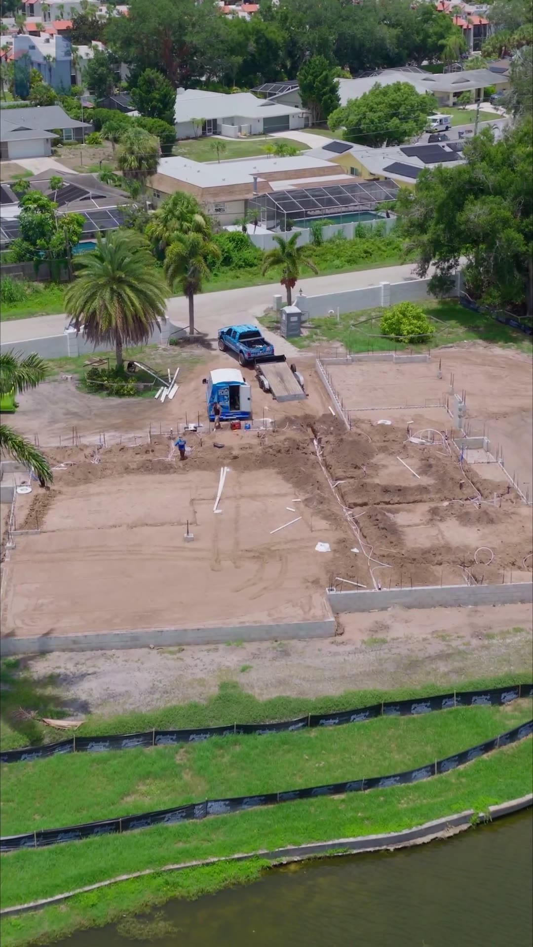 Aerial view of a cleared residential lot with a canal alongside, before plumbing work begins