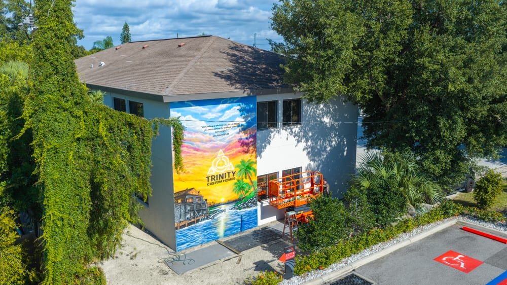 Aerial view of a commercial building with a large painted tropical mural and a lift alongside