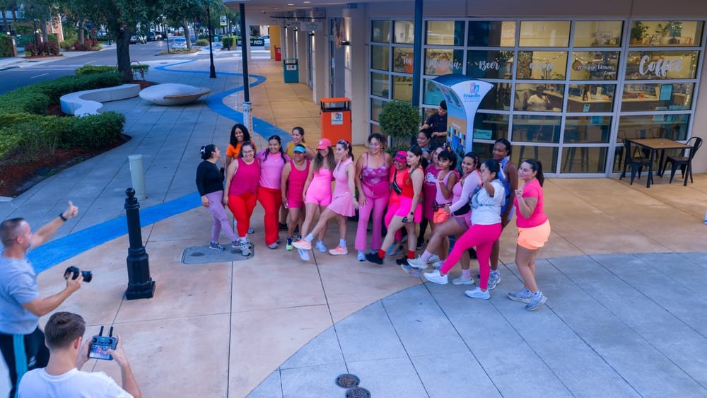 A group in bright activewear posing outside a cafe while a photographer and drone operator work